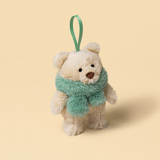 A small plush teddy bear decoration with cream-colored fur, wearing a fuzzy mint green scarf and hanging from a matching green ribbon loop, set against a solid pale beige background. - Image