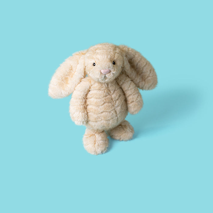 A plush stuffed bunny toy in a light cream or beige color, standing against a solid light blue background. - Image