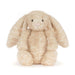 A plush stuffed bunny toy in a soft cream-beige color with long floppy ears, black bead eyes, and a small pink stitched nose, photographed on a clean white background. - Image