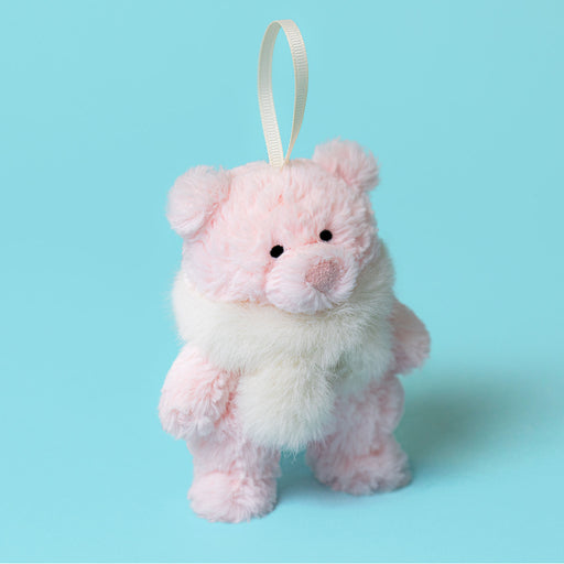 A small plush teddy bear decoration in light pink with a fluffy white faux-fur collar and a cream hanging ribbon, shown on a solid light blue background. - Image
