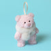 A small plush teddy bear decoration in light pink with a fluffy white faux-fur collar and a cream hanging ribbon, shown on a solid light blue background. - Image