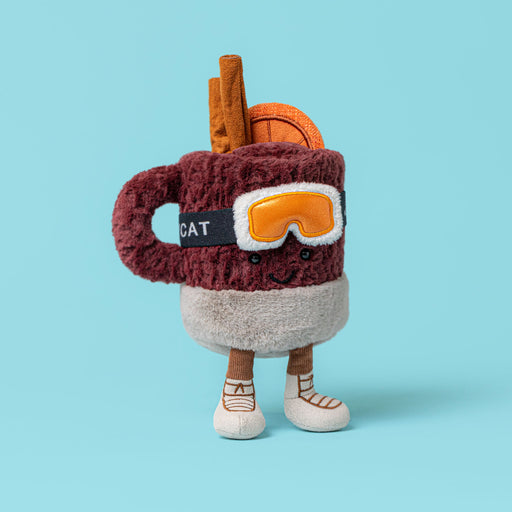Plush soft toy in the shape of a mulled drink in a mug with ski mask and ski boots on. Against a blue backdrop - Image