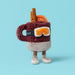 Plush soft toy in the shape of a mulled drink in a mug with ski mask and ski boots on. Against a blue backdrop - Image