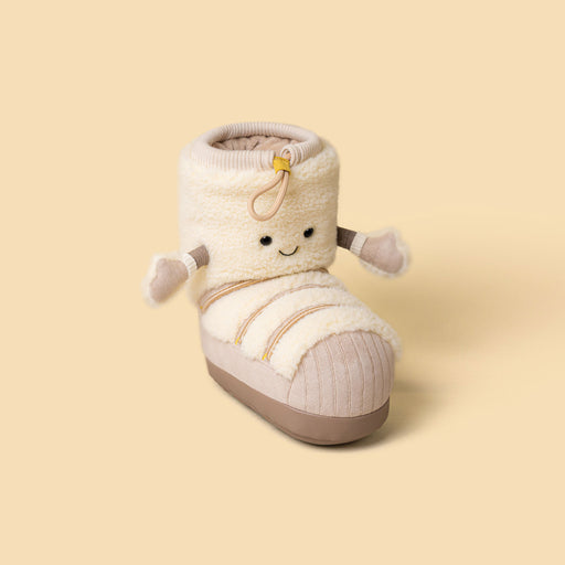 A plush soft toy in the shape of a ski boot in cream and beige with a cute embroidered face and small fabric arms, shown on a solid pale yellow background. - Image