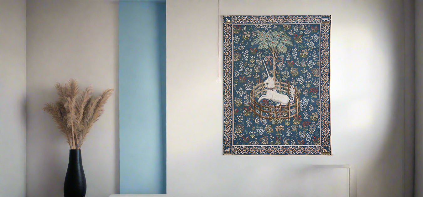 Detailed blue woven tapestry featuring a capative unicorn hangs on a neutral coloured wall.  - Image