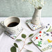 Cup of coffee on a floral coaster with a vase and additional coasters on a table. - Image