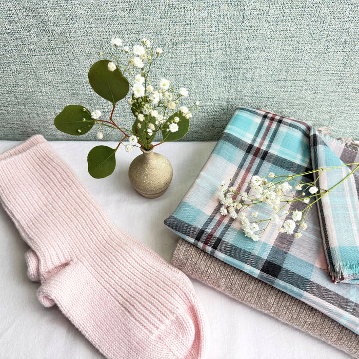 Pink knitted socks, tartan scarf, and small vase with greenery on a textured surface. - Image