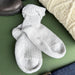 A pair of light grey ribbed knit ankle socks laid flat on a green surface, styled with a cream cable-knit sweater, a dark boot, and blue jeans. - Image
