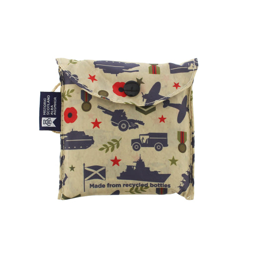 A small fabric pouch with a military-themed print featuring navy blue silhouettes of tanks, ships, and aircraft, red poppy stars, olive green leaves, and a beige background. A black button is on the flap, and a black fabric tag on the left reads 'Recycled Apparel' with a circular logo. - Image