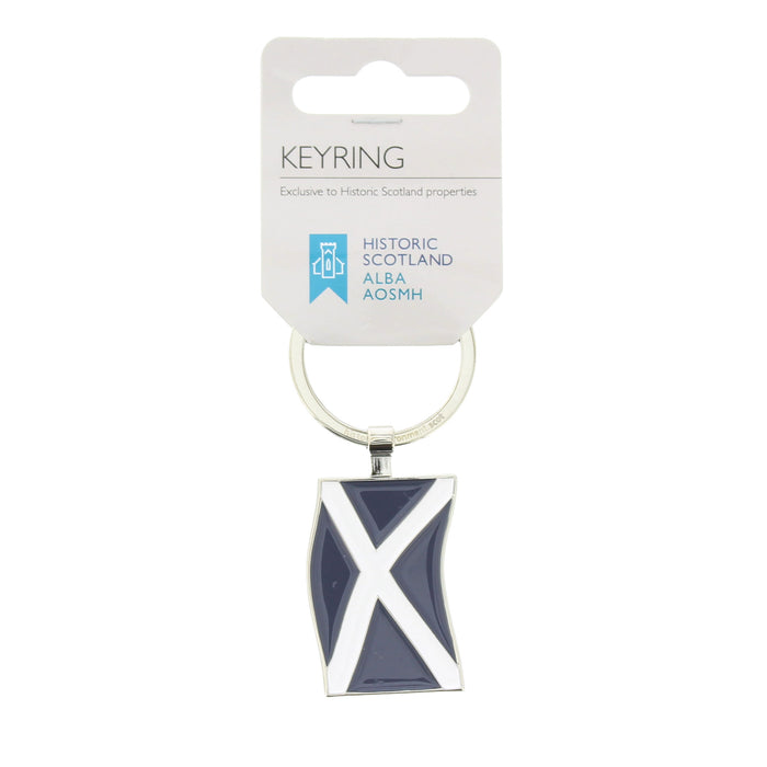 A keyring featuring the Scottish flag (the Saltire) in navy blue and white enamel, attached to a silver metal ring and displayed on a white cardboard hanger card. - Image