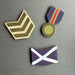 Three wooden military-style magnets arranged on a dark gray background: a chevron rank in olive green and beige, a medal with purple ribbon and gold-toned medallion, and a blue Saltire. - Image