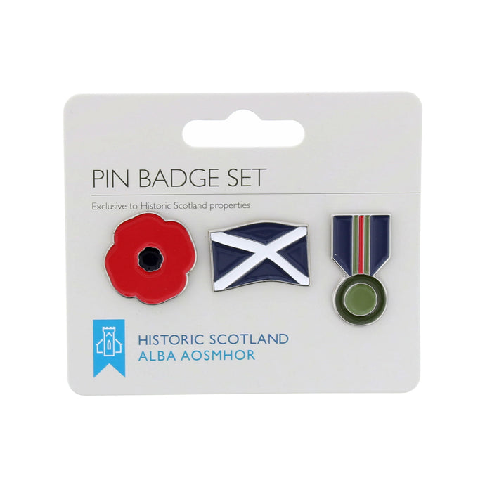 A three-piece pin badge set on a white card backing. The badges include a red poppy flower, the blue and white Scottish flag, and a navy, red and green medal. - Image