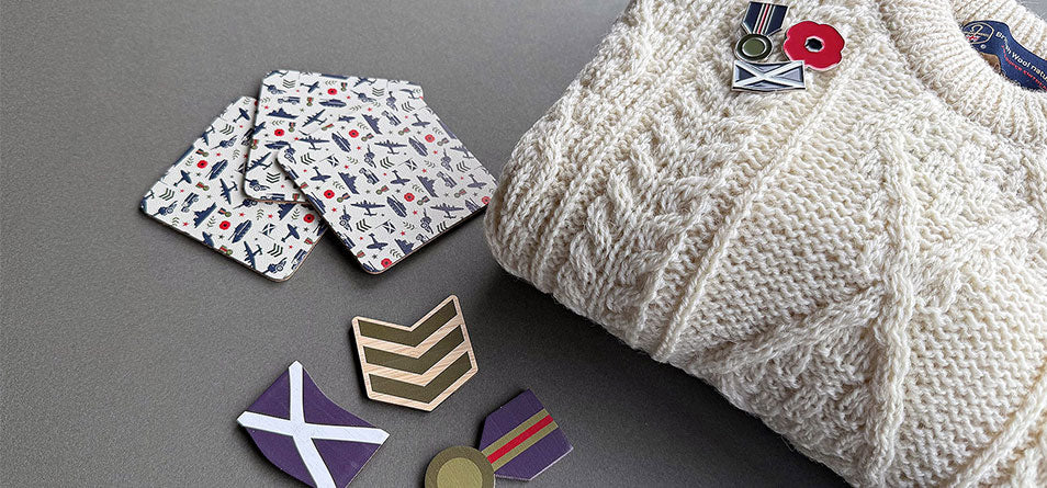 lifestyle image with an Arran sweater with military style pin badges along with military print magnets and coasters.  - Image