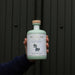 A hand holds a bottle of NcNean Whisky Liqueur against a green door. - Image