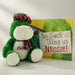 Green plush toy with a tartan scarf next to a book titled 'No Such Thing as Nessie' on a white background - Image