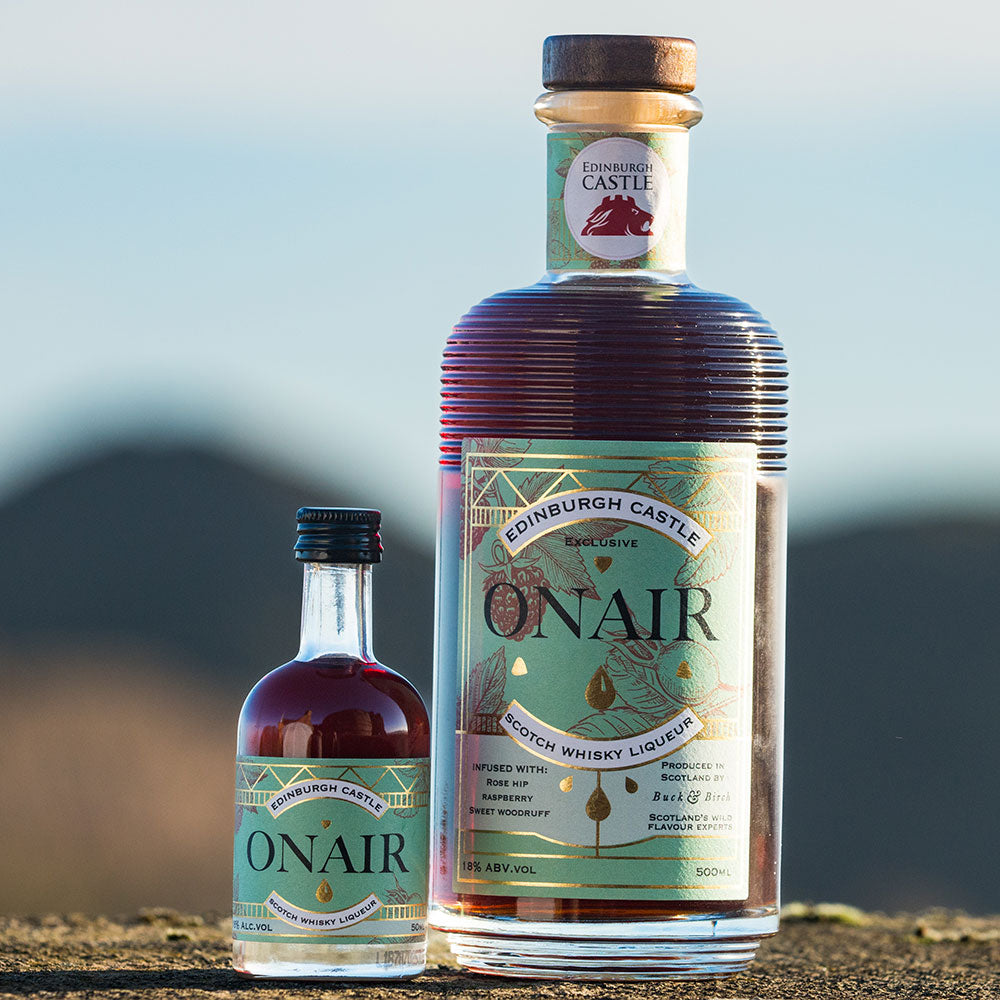 Two bottles of Onair Whisky Liqueur standing outdoors on a stone surface with a blurred mountain and sky background. - Image
