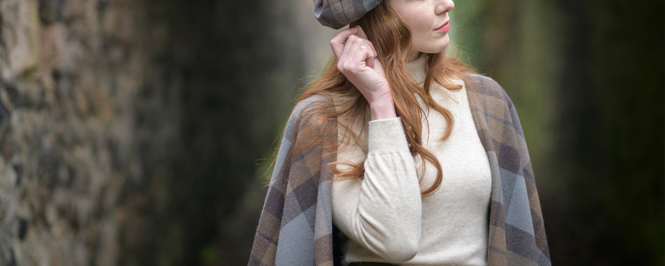Woman wearing an outlander plaid shawl and hat in a darkened walled path - Image