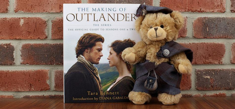 Teddy dressed in outlander tartan with a hardback book about the series.  - Image