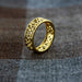 Gold ring with intricate design on a textured surface - Image