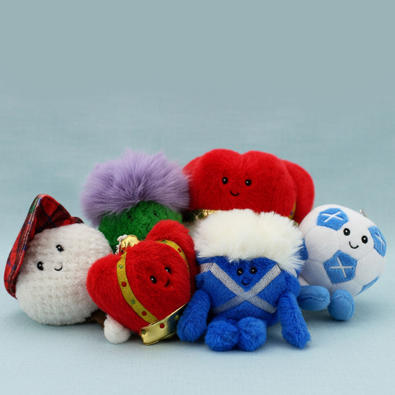 A group of six colorful plush keychains shaped like Scottish-themed characters, all arranged on a light blue background. - Image