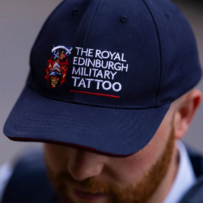 A close-up of a man wearing a navy blue baseball cap with white embroidered text reading 'THE ROYAL EDINBURGH MILITARY TATTOO' and a small crest on the front. - Image