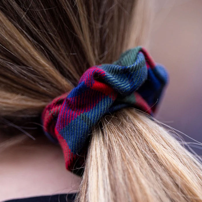 A close-up of a person's blonde hair tied up in a low ponytail with a plaid fabric scrunchie. The scrunchie features a tartan pattern in red, blue, and green. - Image