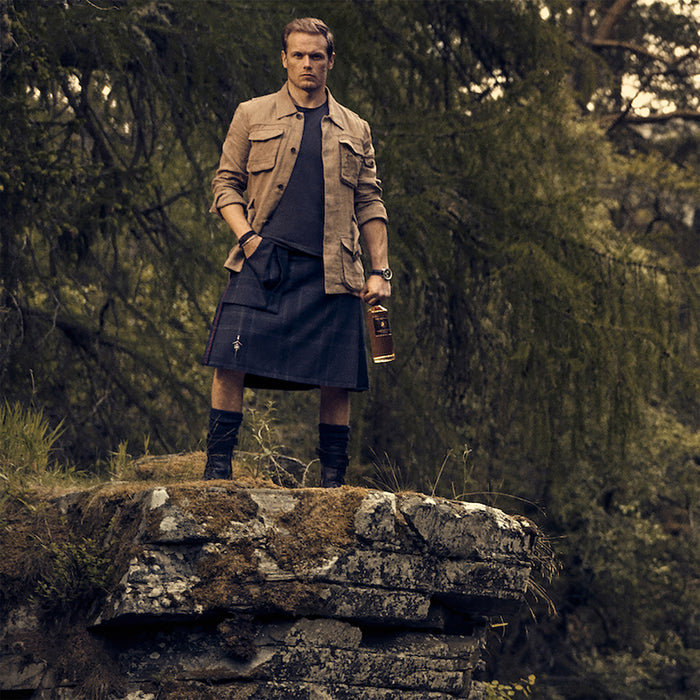 Man in a kilt standing on a rock in a forest - Image