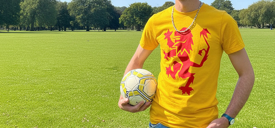 Person wearing a yellow t-shirt with a red Lion Rampant design, holding a football on a grassy field. - Image