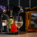 Bottle using the Stag Bottle Pourer pouring white wine into a glass with bottles in the background - Image