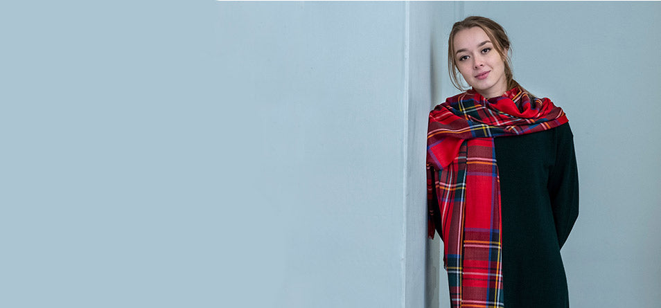 person leans against a blue wall wearing a red tartan scarf - Image