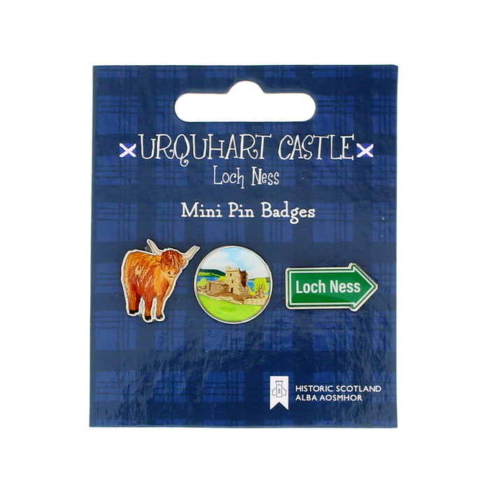 Packaging of Urquhart Castle Loch Ness mini pin badges with a highland cow, loch scene, and green arrow. - Image