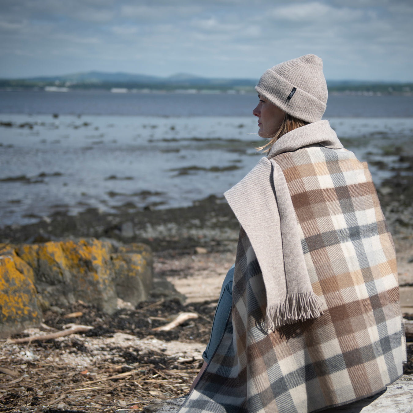 Person wearing the castle cosies range and a tartan blanket looks out over a autumnal seascape. 