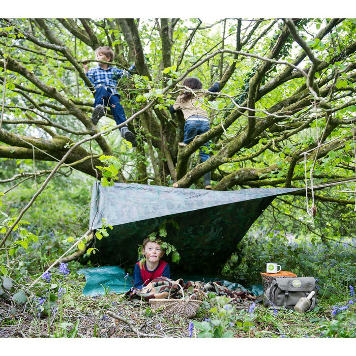 Children playing in a tree with the den kit set up and foliage on the ground 