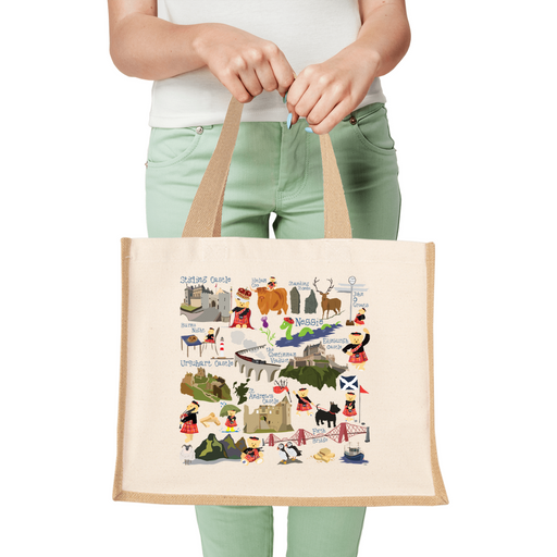 Person wearing green jeans holds a jute shopper that features Piper Bear and various Scottish landmarks 