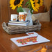 Autumn Highland Cow Tablemat shown at angle on table with other items from the collection including a mug and coaster with sunflowers in the background