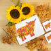 Autumn Highland Cow Tablemat shown from above on table with leaves and sunflowers
