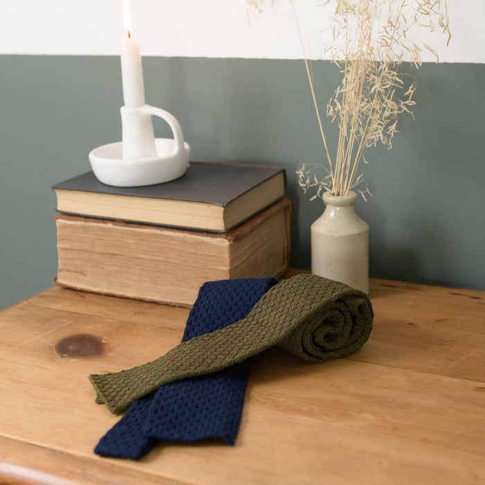 Honeycombe Tie Navy shown with bracken green tie from the same range on bedroom dresser top next to a candle and some books