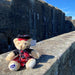 Scottish Dressed cuddly teddy bear sits on a wall in front of Stirling Castle on a sunny day. 