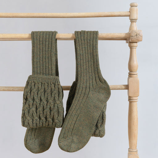 Green heavy wool knee high socks are hanging over a wooden drying rail 