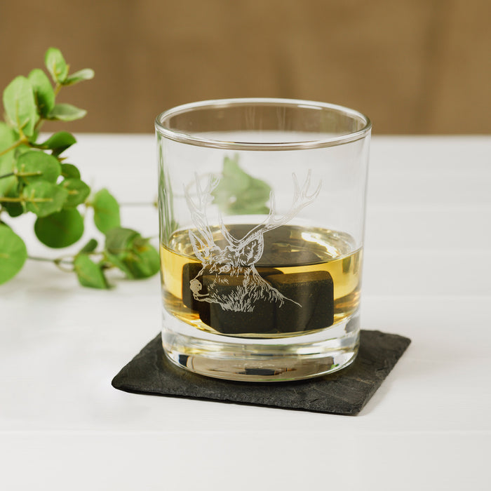 close up view of single glass with stag etched in glass on a slate coaster for context 