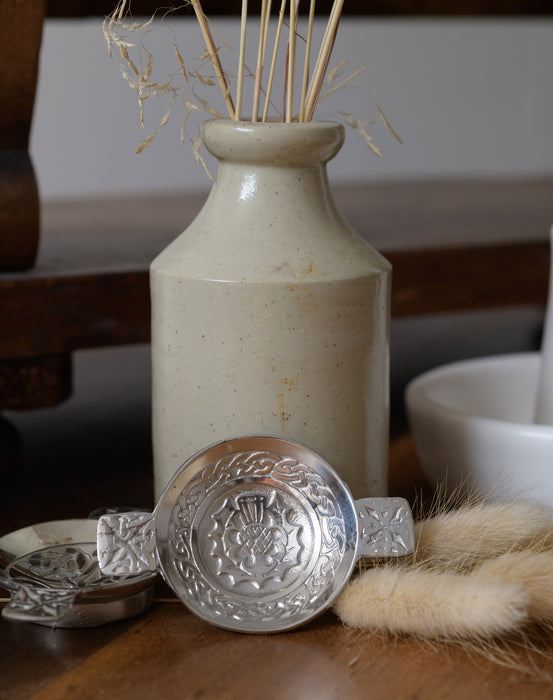 Quaich Mini Thistle shown propped against traditional vase on table with dried grasses